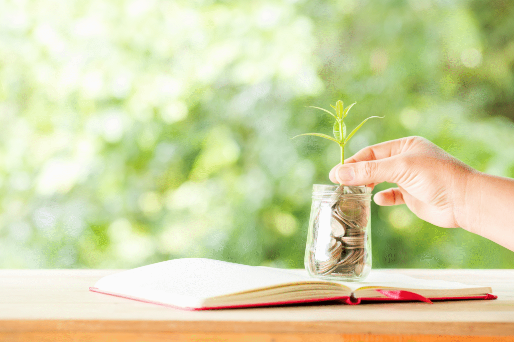 A jar of money on a book, with a plant growing out of it